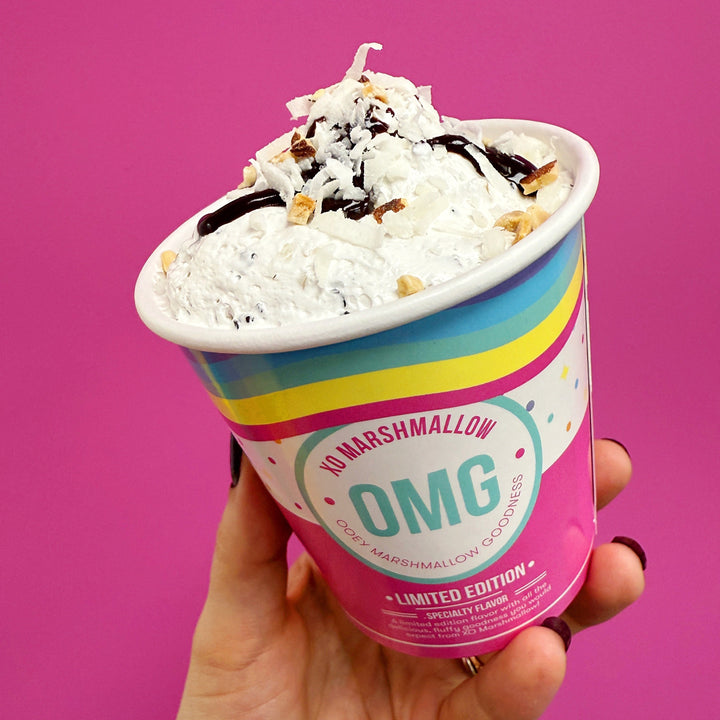 hand holding a pint of almond joy marshmallow creme against a pink background