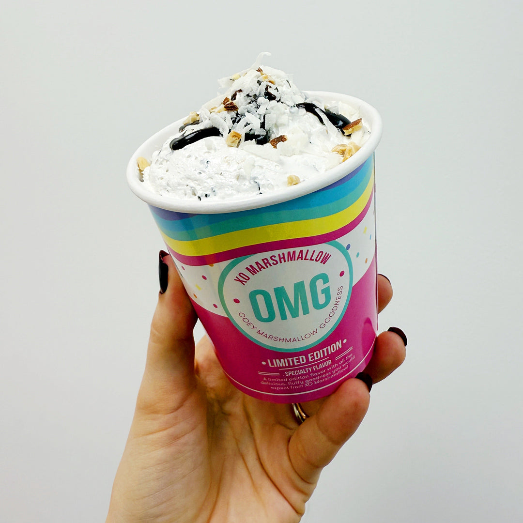 hand holding a pint of almond joy OMG topped with coconut and chocolate against a white background