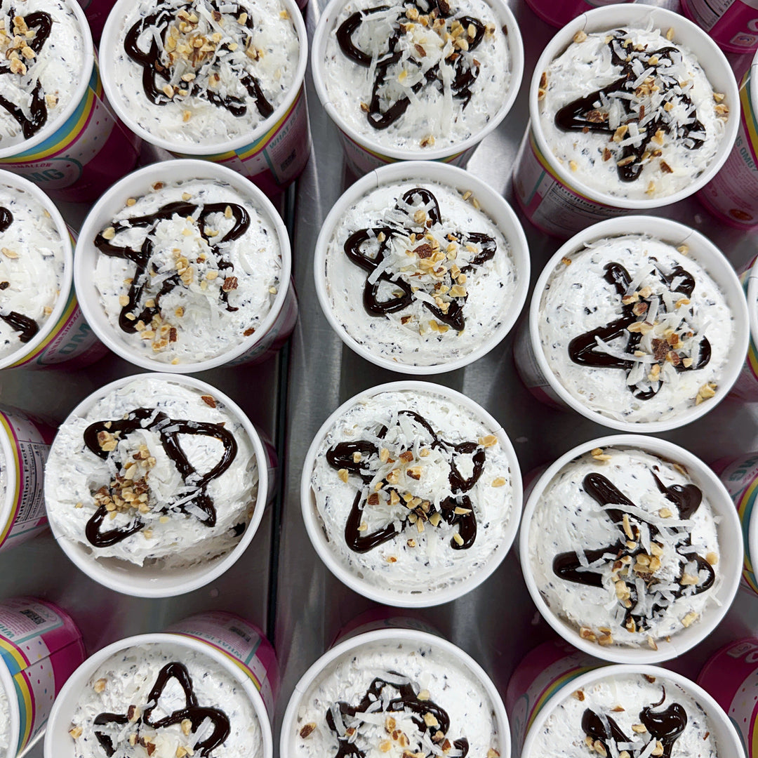 Multiple small dessert cups with marshmallow fluff, chocolate drizzle, and nuts arranged in rows.