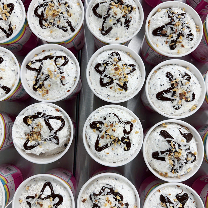 Multiple small dessert cups with marshmallow fluff, chocolate drizzle, and nuts arranged in rows.