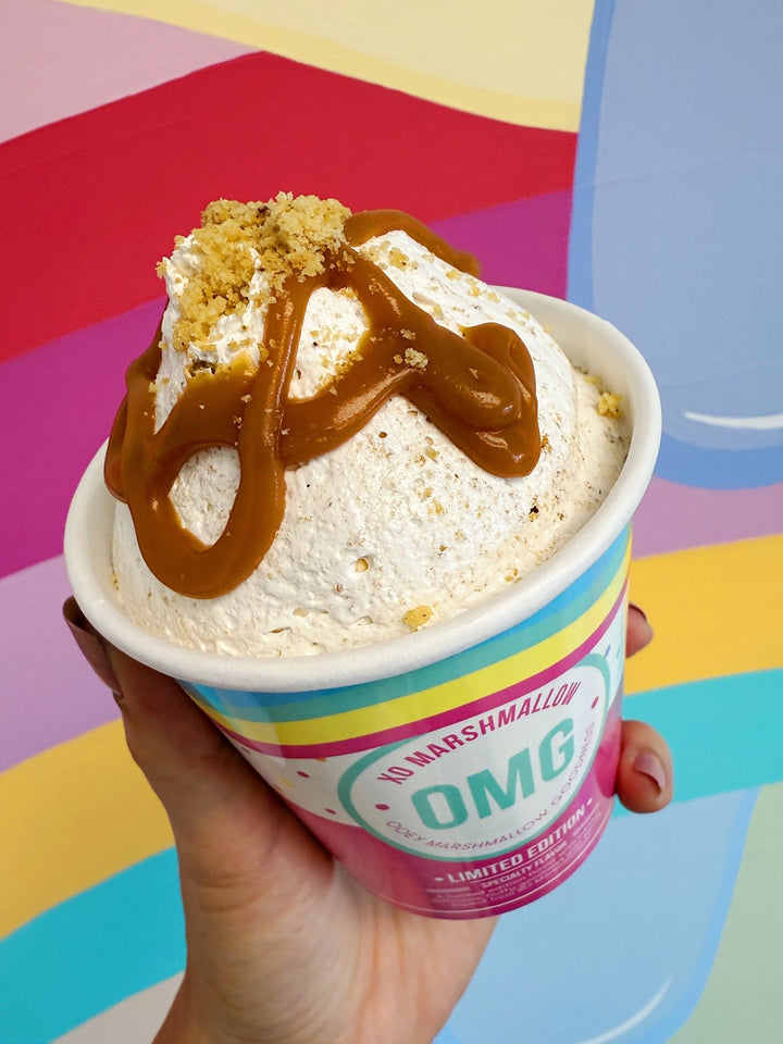 Marshmallow fluff with butterscotch drizzle and brown butter cookie pieces in a colorful container held against a multicolored background.