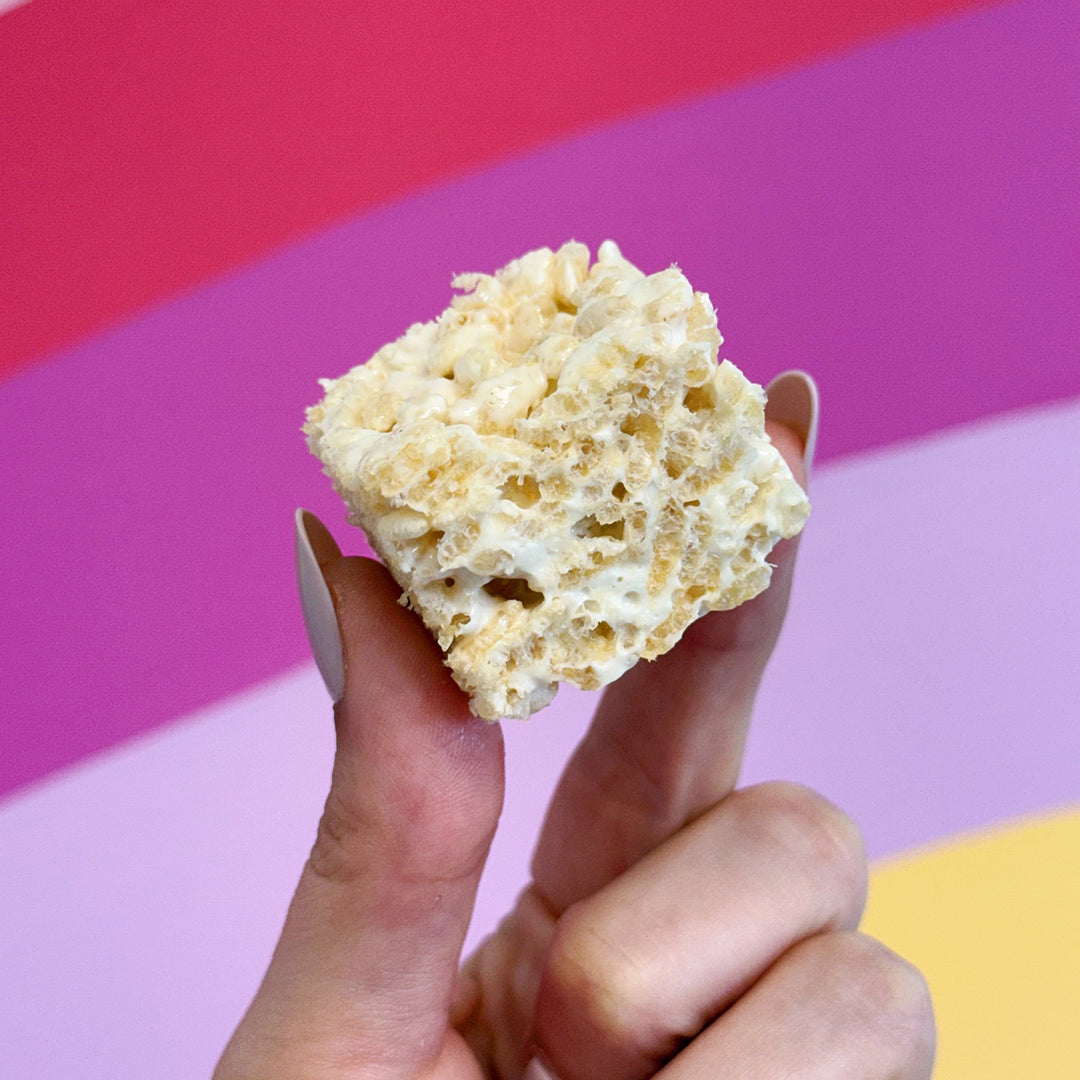 Hand holding a rice krispies treat against a colorful striped background