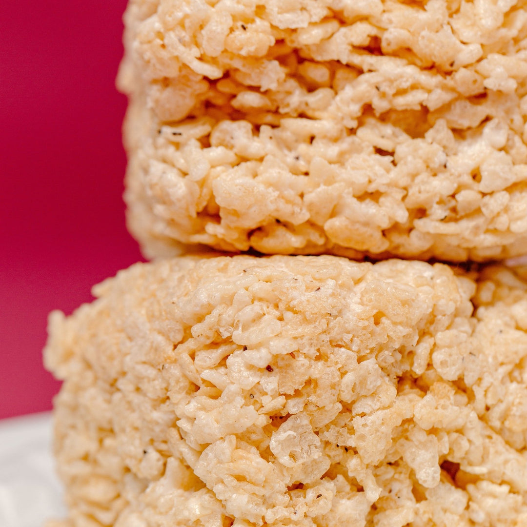 A stack of gluten free bite sized rice crispy treats from XO Marshmallow against a red/deep pink background