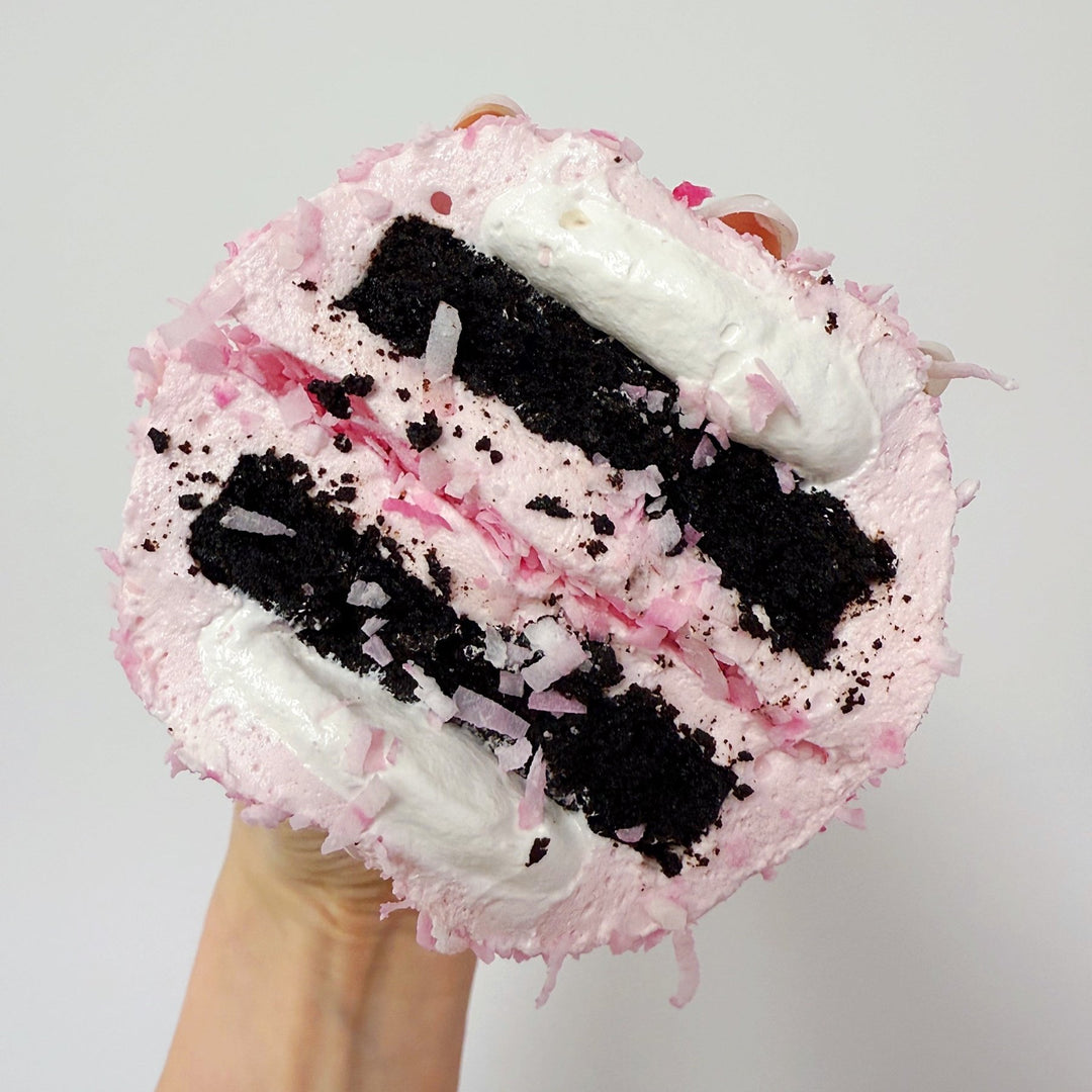 A cross section of a XO marshmallow bonbon held against a white background, with layers of coconut marshmallow, marshmallow fluff and gluten free brownie visible. This photo really shows all of the layered details of the treat. It's similar to a SnoBall.