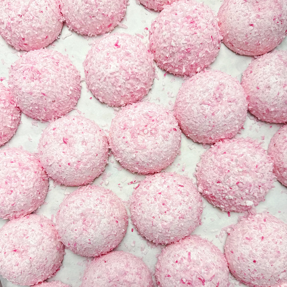 An overhead shot of a tray of pink domes covered in shredded coconut. These are the XO Marshmallow Coconut Cake BonBombes.