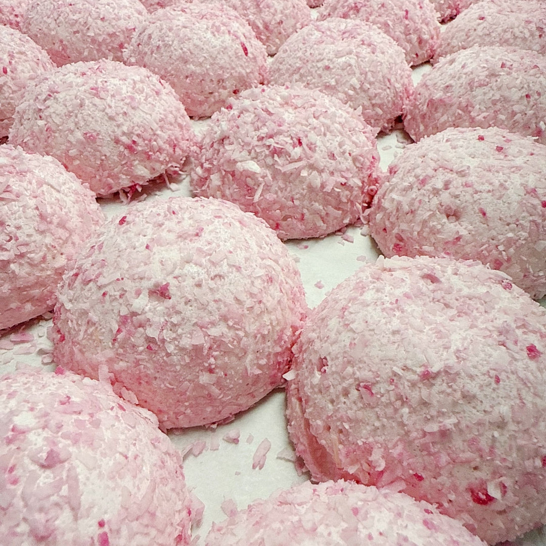 A detailed shot of the Coconut Cake Bonbombes on a tray. Similar to a SnoBall, you see pink domes covered in a shredded pink coconut. It's a natural food coloring not an artificial dye.
