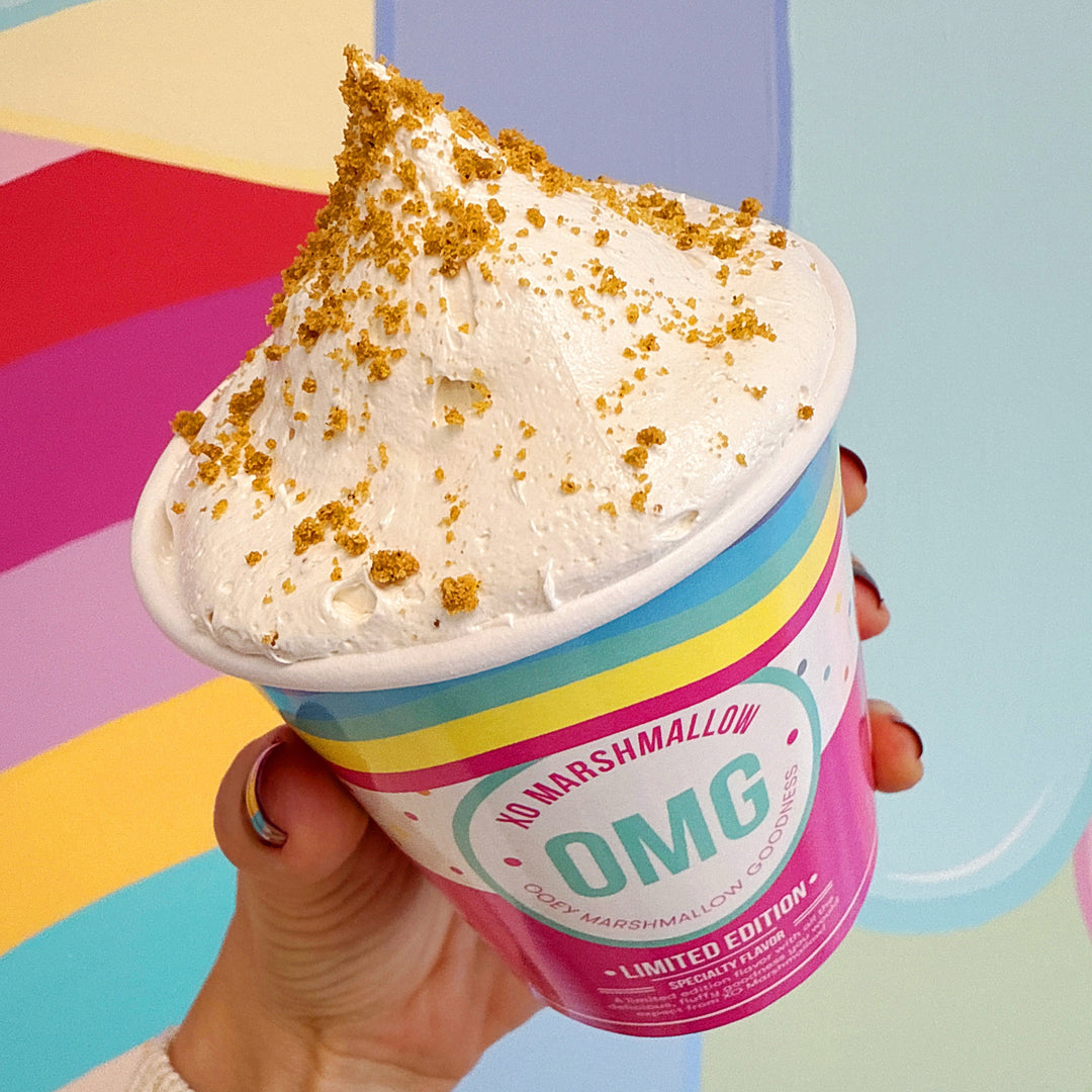 Hand holding a container of gluten free cookie butter marshmallow spread with colorful background