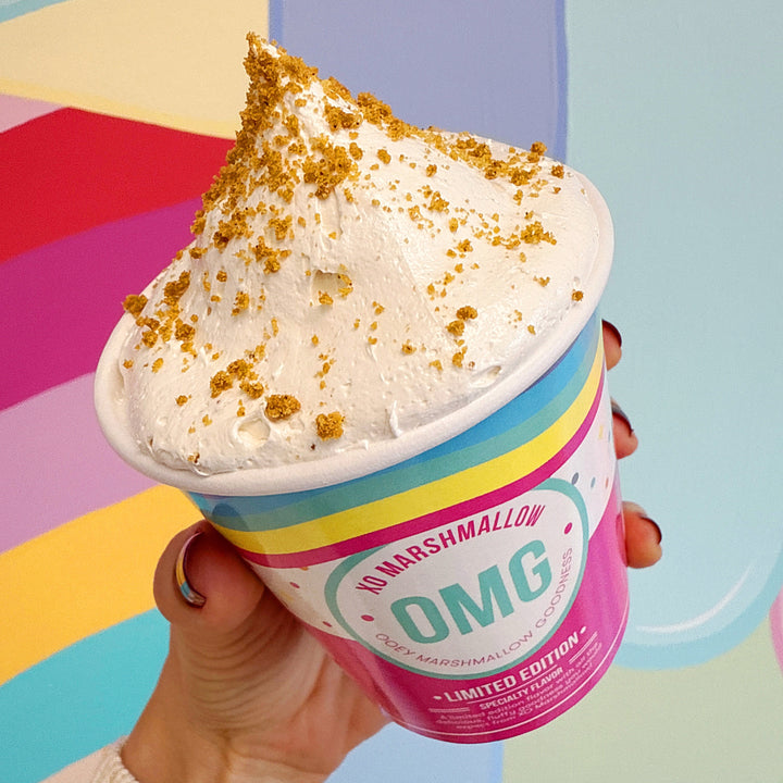 Hand holding a container of gluten free cookie butter marshmallow spread with colorful background