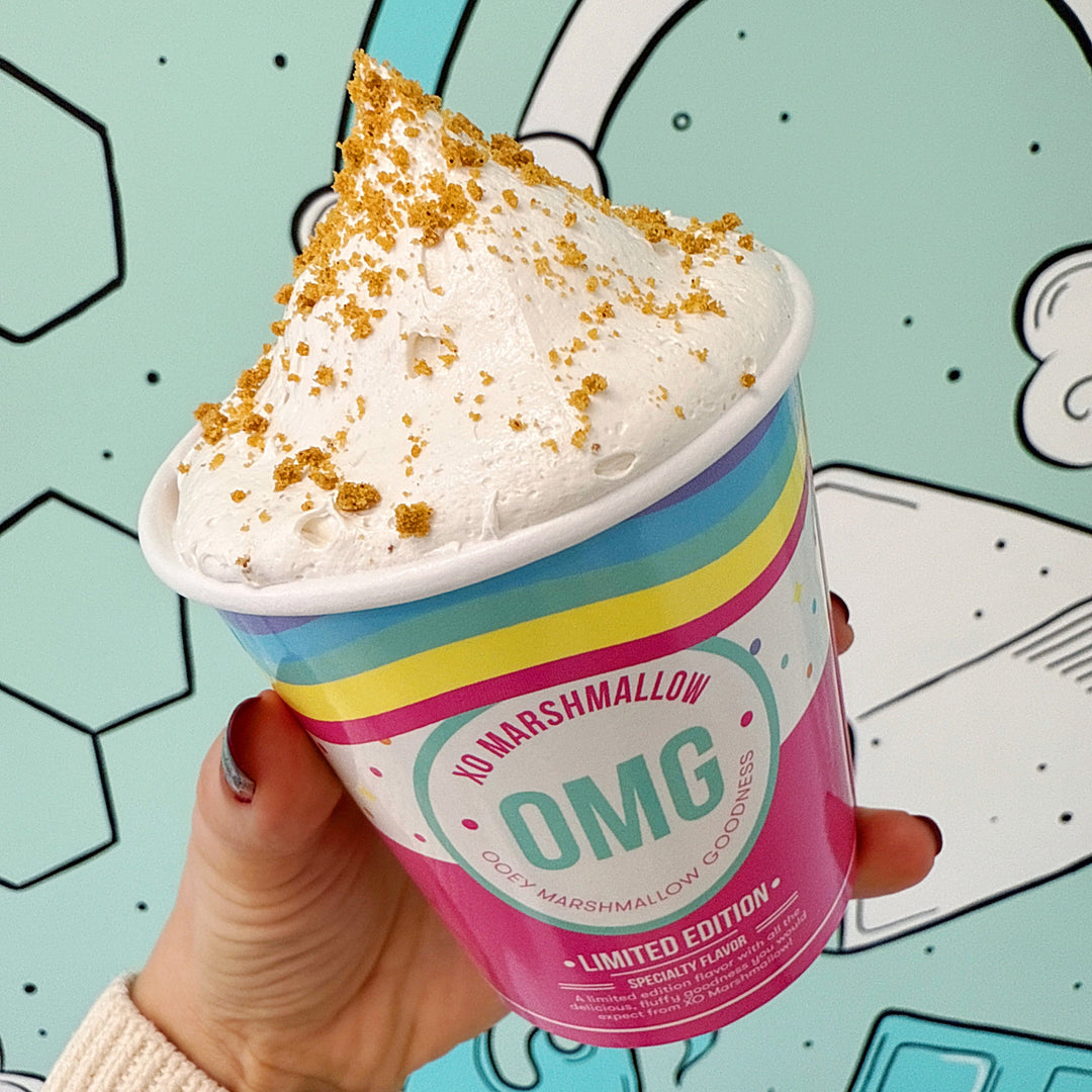 Hand holding a colorful cookie butter marshmallow fluff container with 'OMG' branding against a playful background
