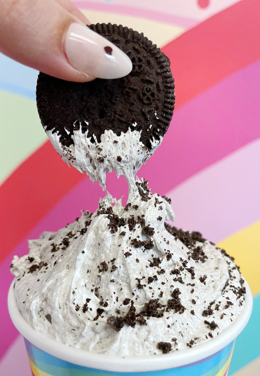 A hand with cute nails dipping a gluten free chocolate sandwich cookie into a pint of Vegan Cookies and Cream Marshmallow Fluff from XO Marshmallow.