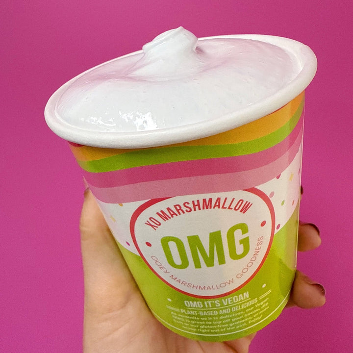 Hand holding a pint of vegan cotton candy flavored marshmallow creme on a pink background