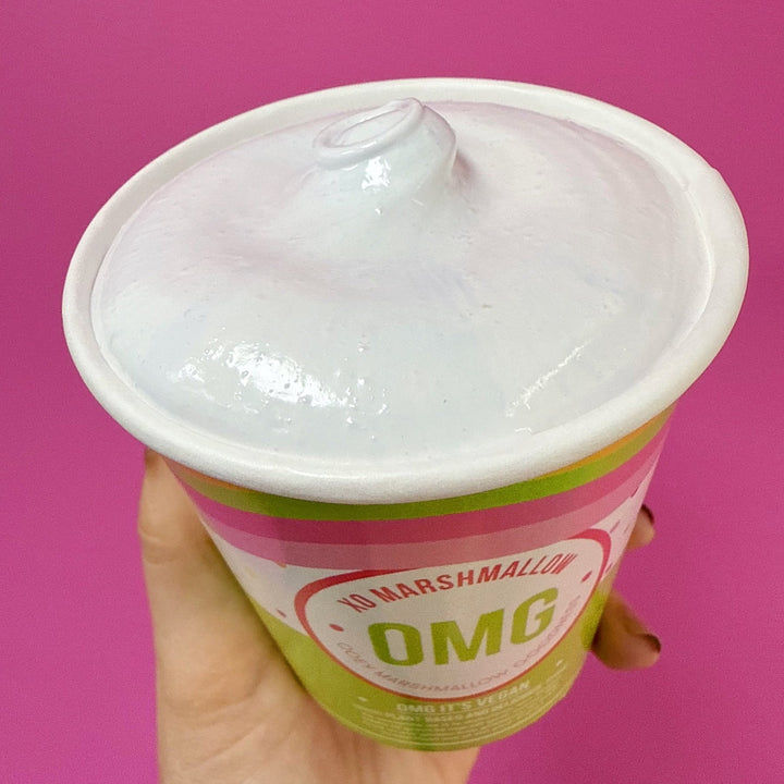 Hand holding a pint of cotton candy flavored marshmallow fluff using natural food coloring against a pink background