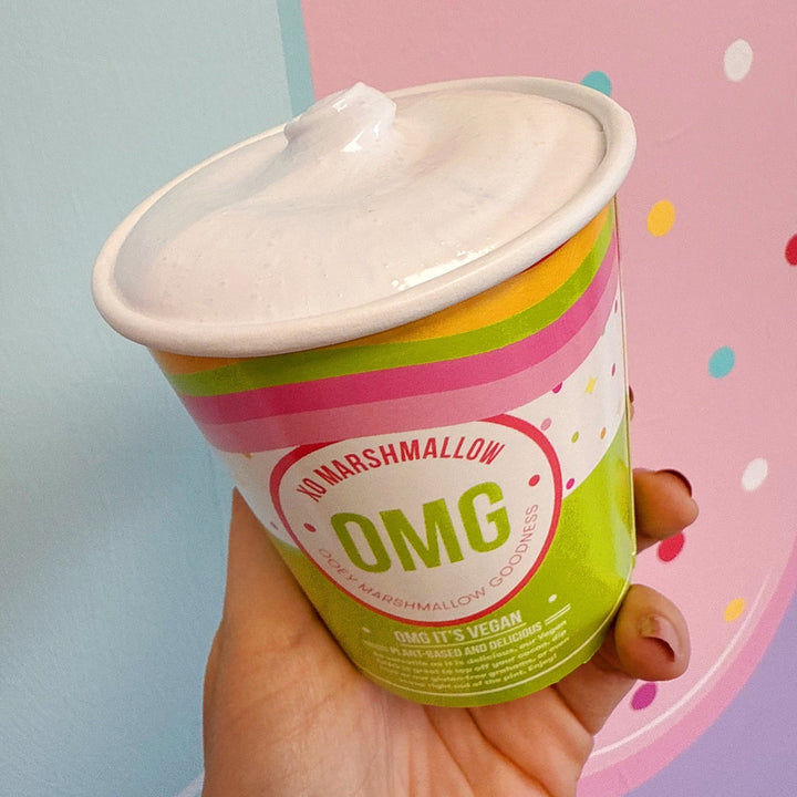Hand holding a colorful container of vegan cotton candy marshmallow spread with a pink background
