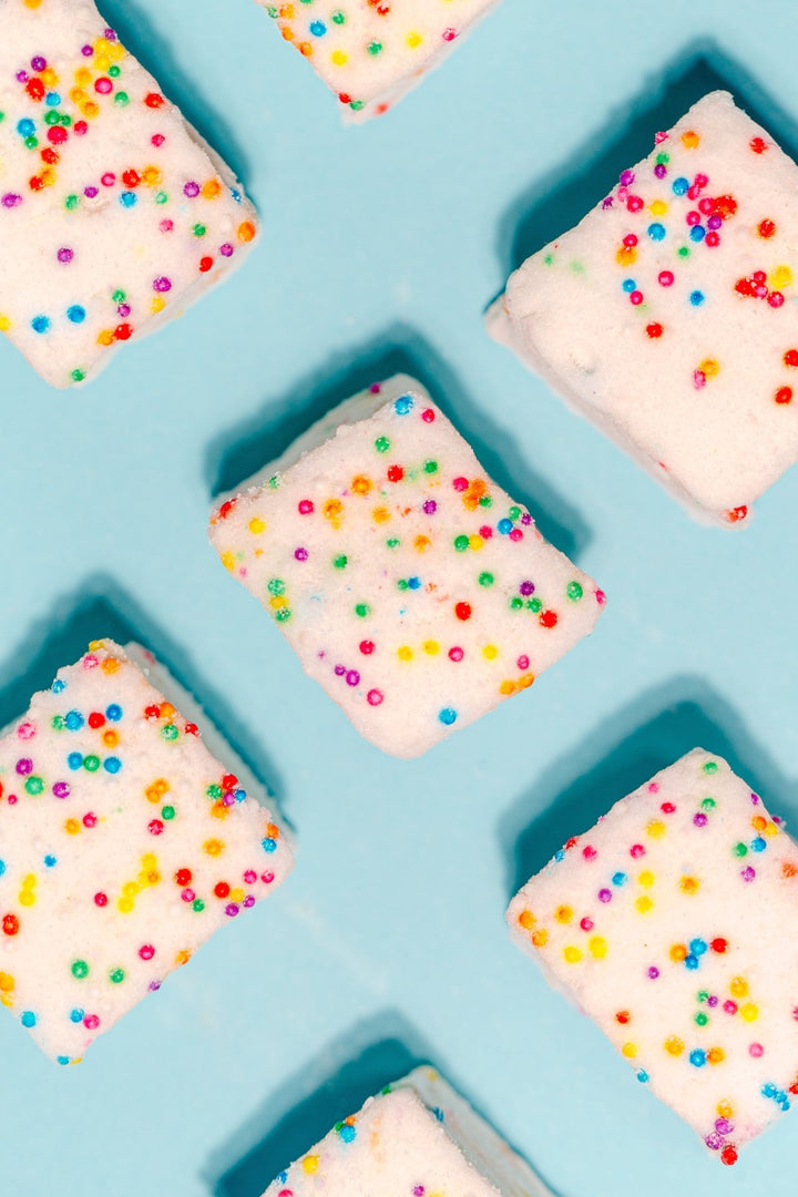 An overhead grid photo of the Funfetti homemade marshmallows against a blue background. All of the marshmallows are covered in natural dye sprinkles.
