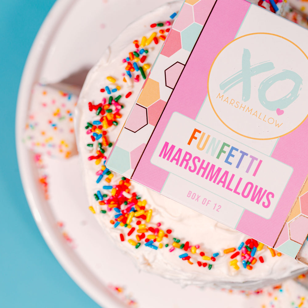 A close up of the colorful packaging for Funfetti Marshmallows on top of a birthday cake with lots of sprinkles.