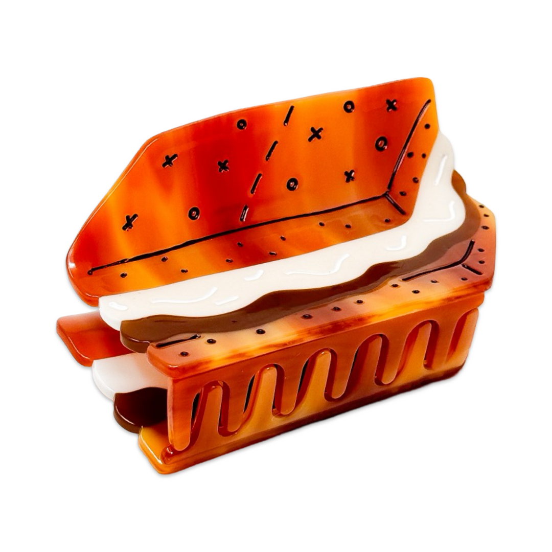 A hair claw clip in the shape of a s'mores design, featuring white marshmallows and a red and yellow pattern resembling a s'mores treat.