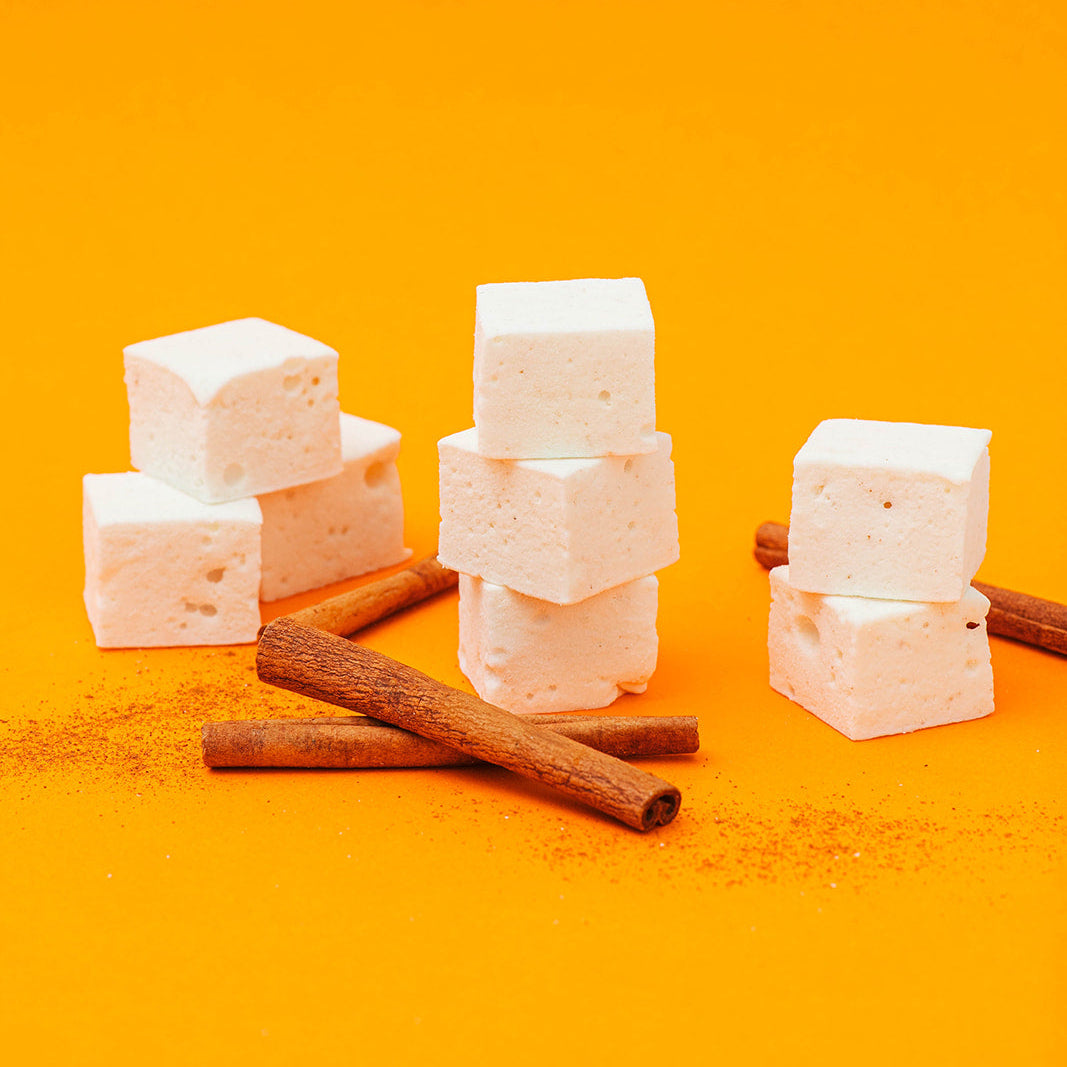 maple cinnamon marshmallows and cinnamon sticks arranged on a bright orange background.
