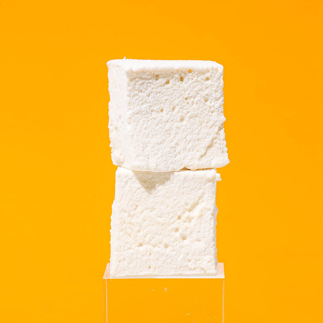 Two Maple Cinnamon marshmallows displayed on a clear acrylic stand against a solid bright orange background.