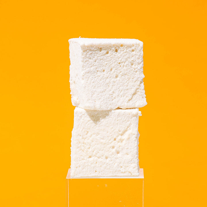 Two Maple Cinnamon marshmallows displayed on a clear acrylic stand against a solid bright orange background.