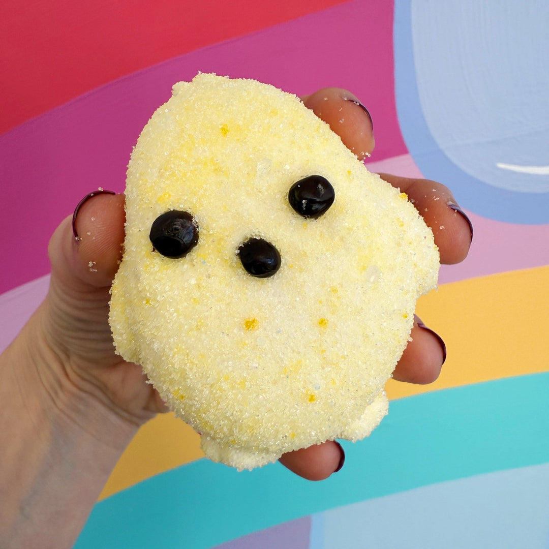 Hand holding a yellow marshmallow chick against a colorful background