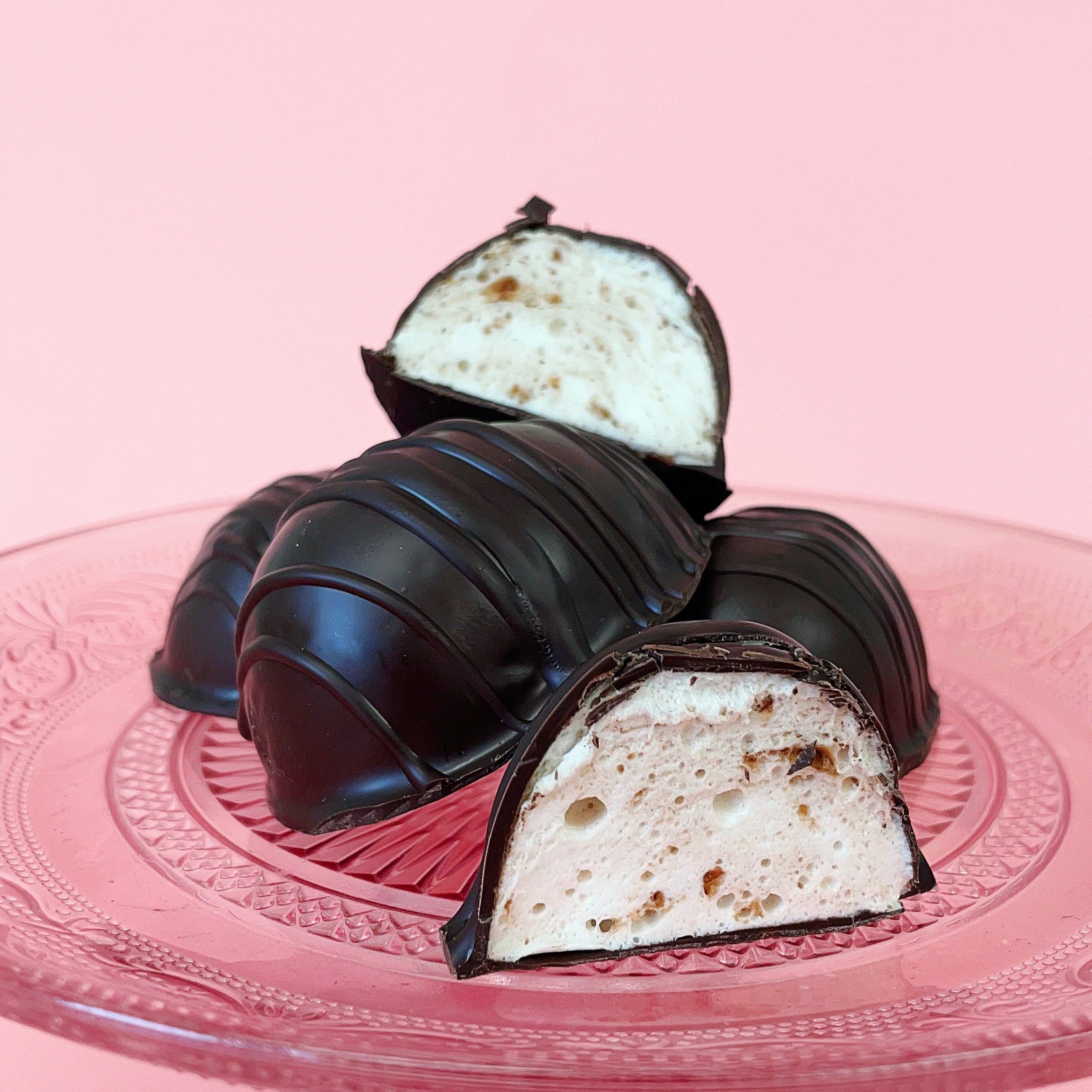 Two chocolate covered eggs, one with a dark chocolate coating and the other with a light, fluffy marshmallow filling visible in the center.