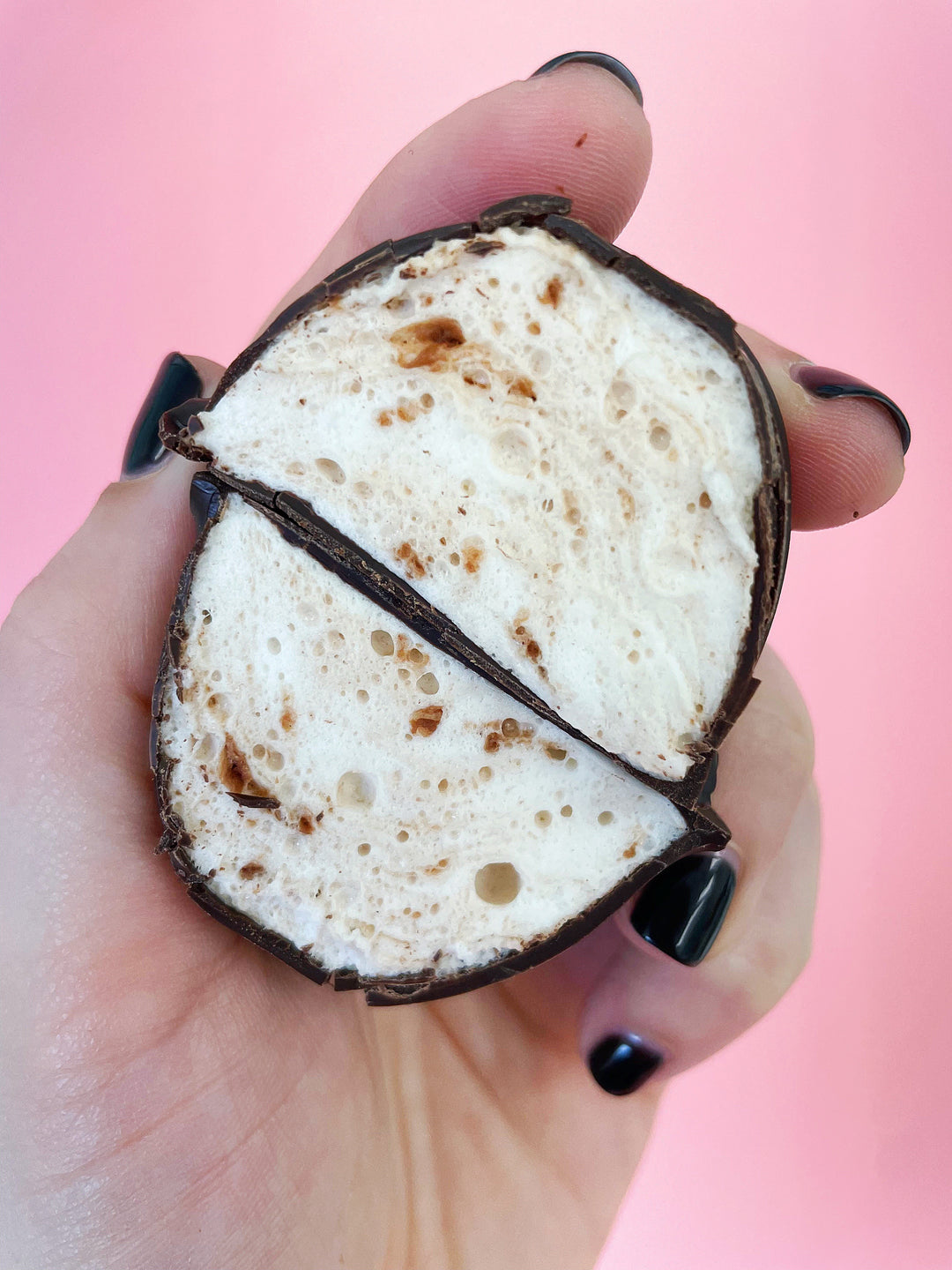 Another angle of a hand holding an easter egg shaped nutella flavored marshmallow that has been cut in half. The entire egg is coated in chocolate. 