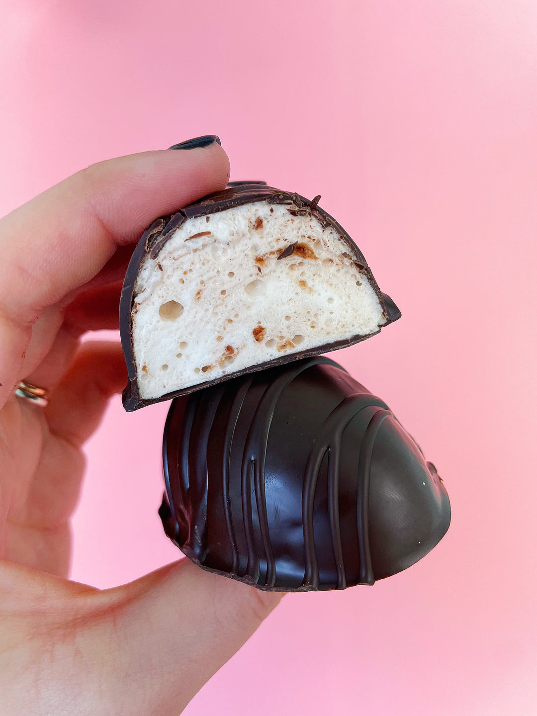 A hand holding an uncut chocolate covered egg and half of a cut egg. The cut egg has a nutella marshmallow filling.