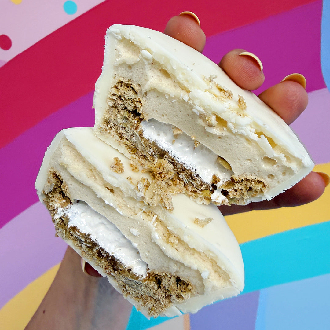 A hand holding two halves of a white chocolate and waffle sandwich cookie, showing the layered waffle and cream filling, set against a colorful abstract background.