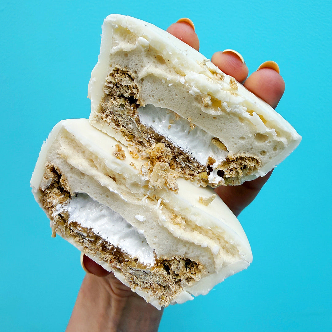 A hand holding two halves of a white chocolate and cookie sandwich pastry against a bright turquoise blue background.