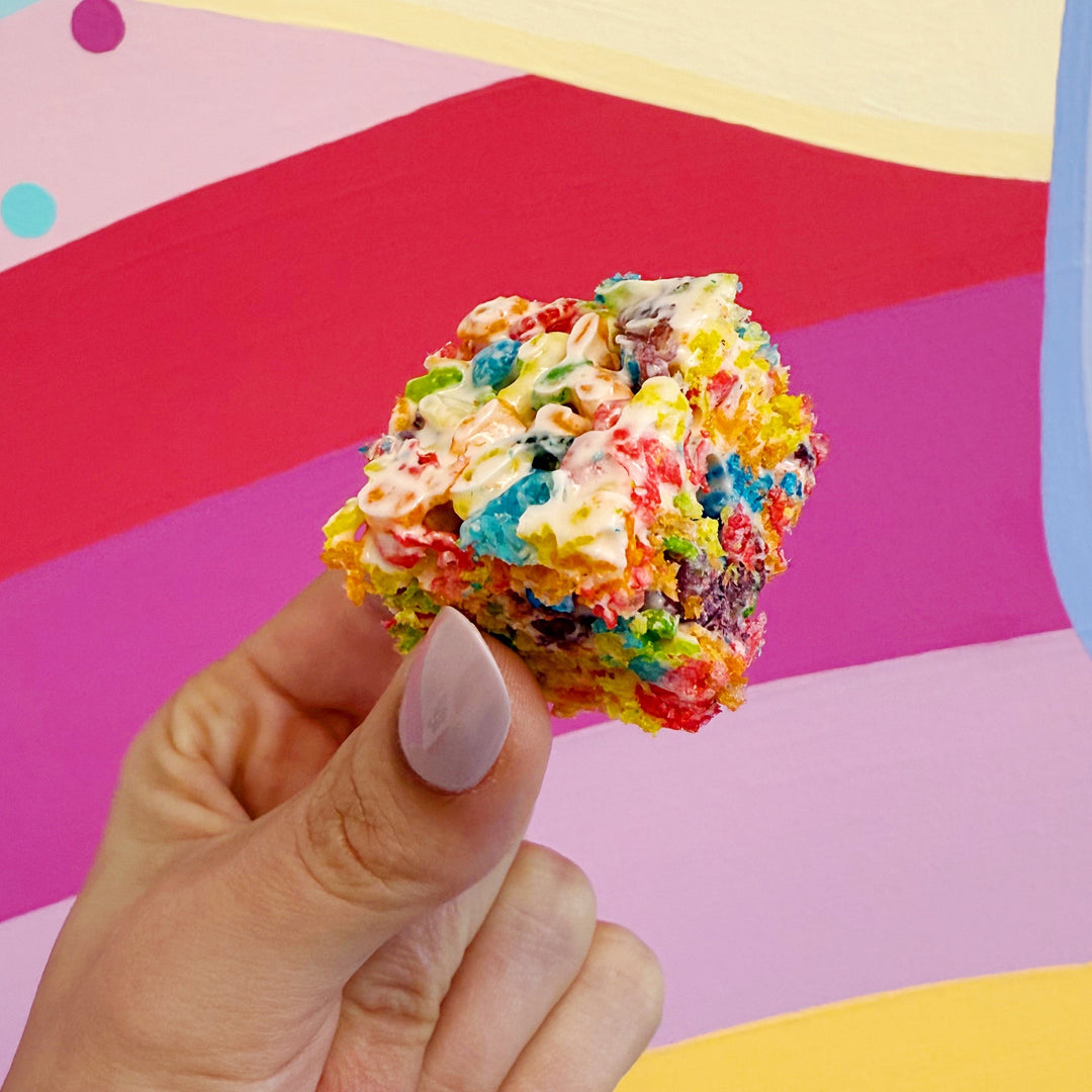 Colorful cereal treat held by a hand against a multicolored background