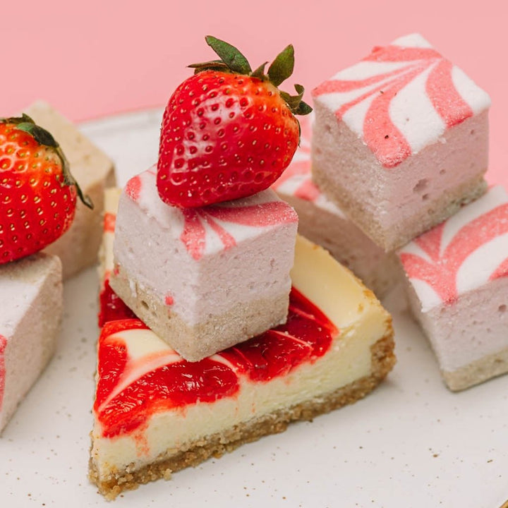 Square strawberry cheesecake gourmet marshmallows sitting on top of a slice of cheesecake with a pink background