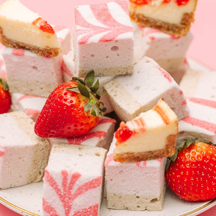 Square strawberry cheesecake marshmallows with whole strawberries on a pink background