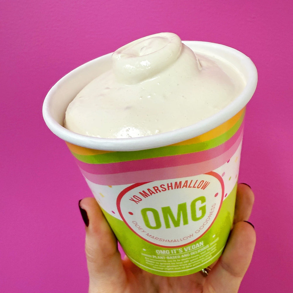 Hand holding a pint of vegan salted caramel marshmallow fluff against a bright pink background
