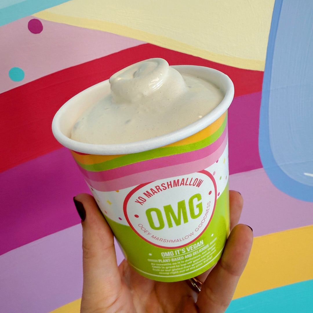 A hand holding a pint of vegan salted caramel ooey marshmallow goodness against a rainbow background