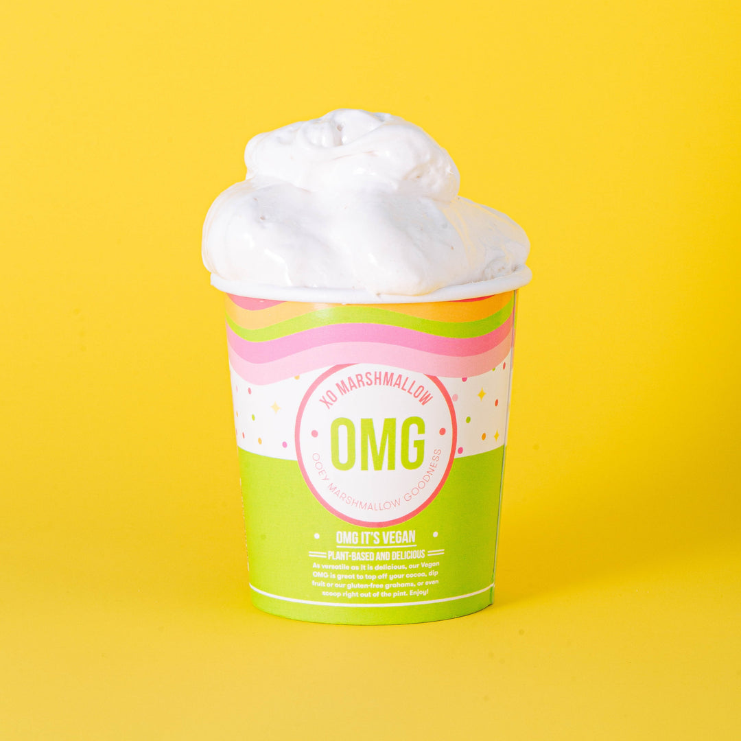 A pint container of Vegan Vanilla OMG marshmallow creme with a large scoop of marshmallow on top, presented on a yellow background.