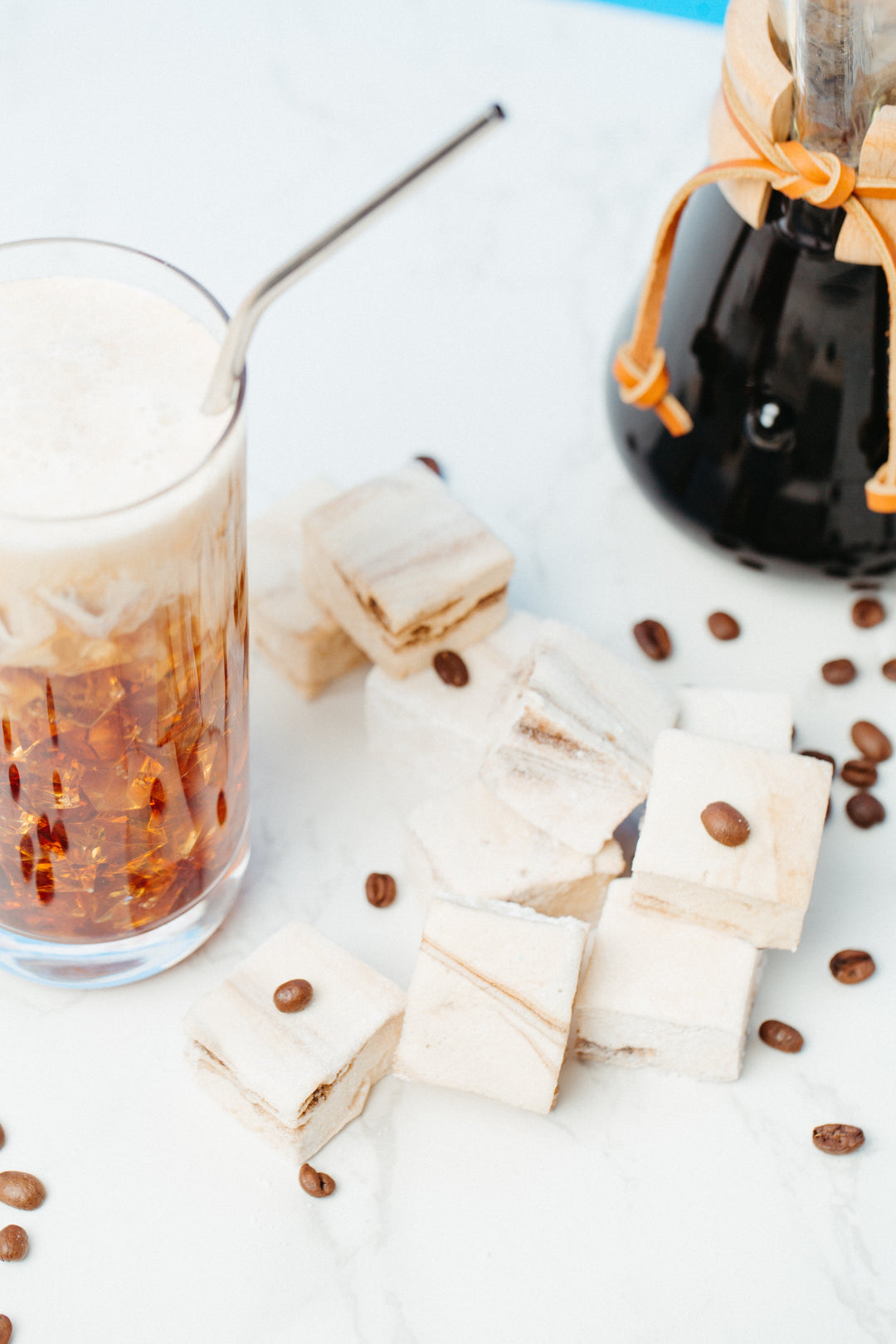 An overhead shot of a glass of iced coffee and caffeinated marshmallows against a marble background