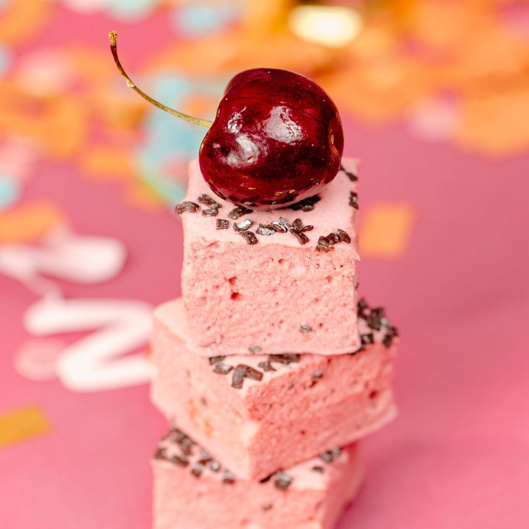 Cherry Marshmallows with chocolate pieces on top of them stacked in a pile with a bright cherry on top