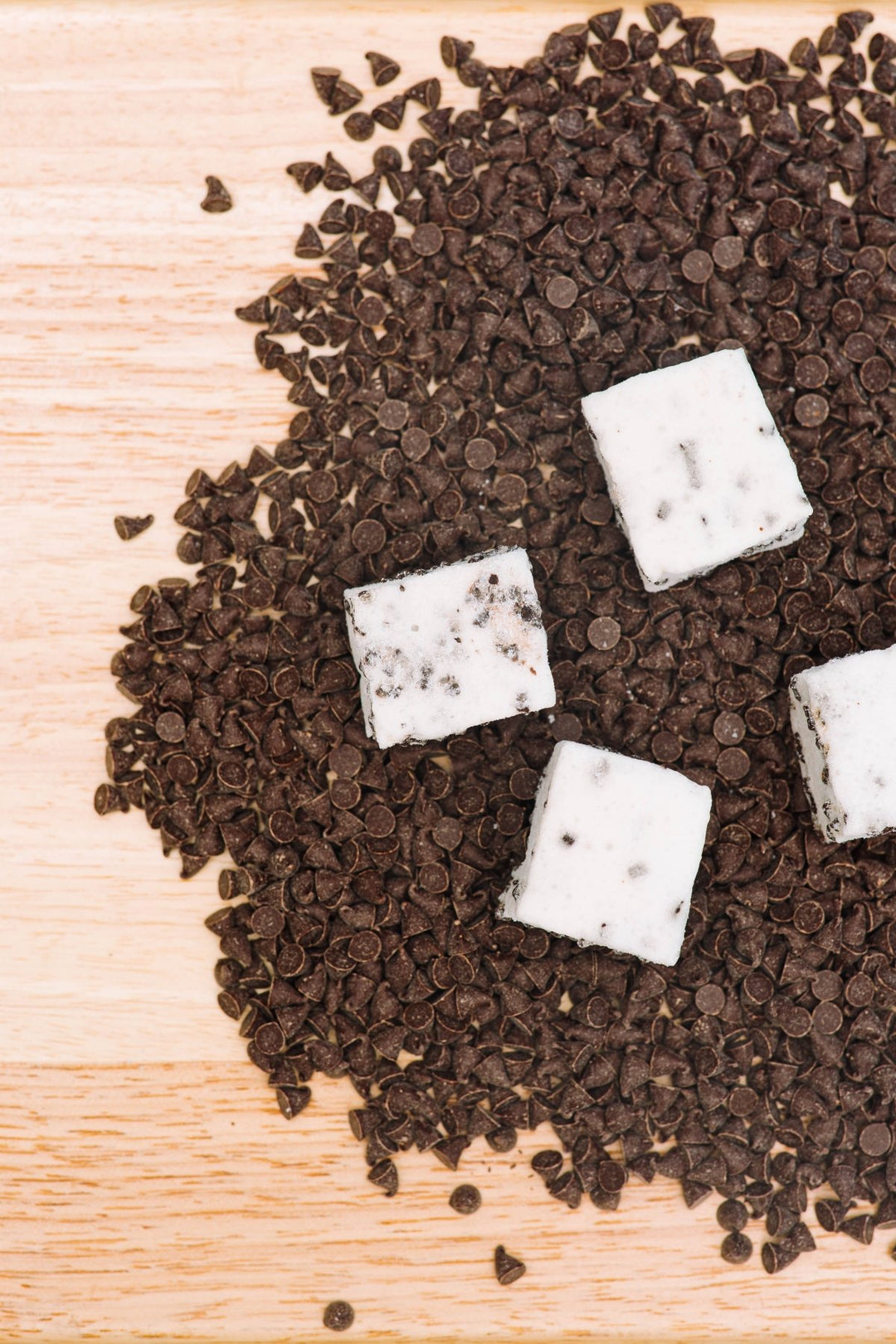 A wooden cutting board covered in a large pile of chocolate chips with 4 gourmet XO Marshmallow chocolate chip marshmallows on top of them.