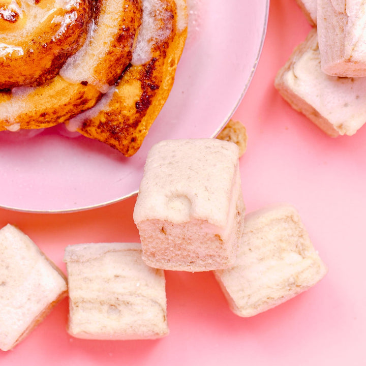 A close up photo of 3 gourmet XO Marshmallow gluten free cinnamon roll marshmallows next to a plate with a cinnamon roll on it.