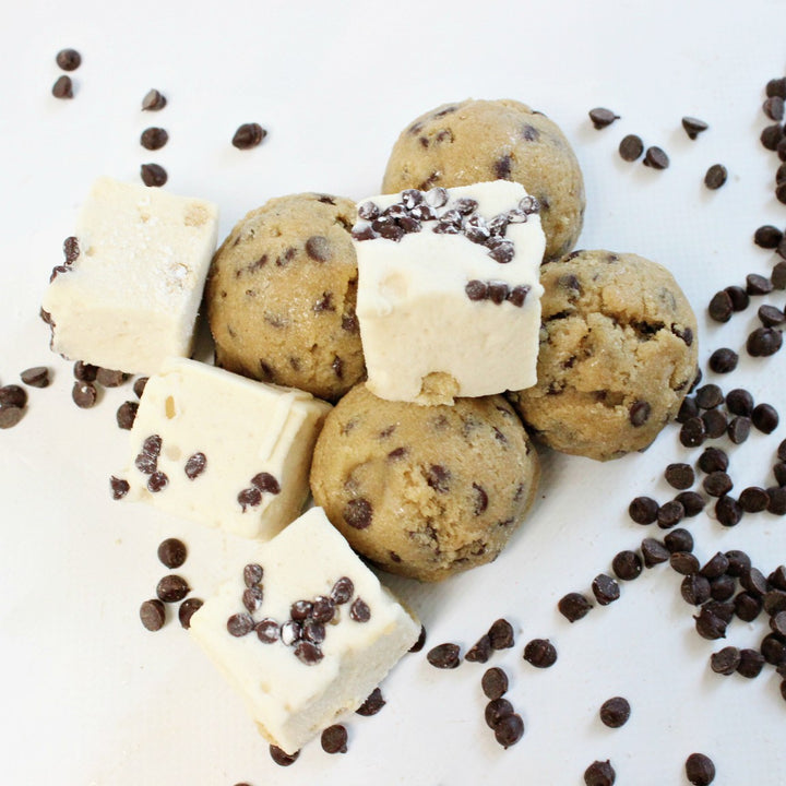 scoops of gluten free cookie dough surrounded by cookie dough favored marshmallows and chocolate chips scattered against a white background