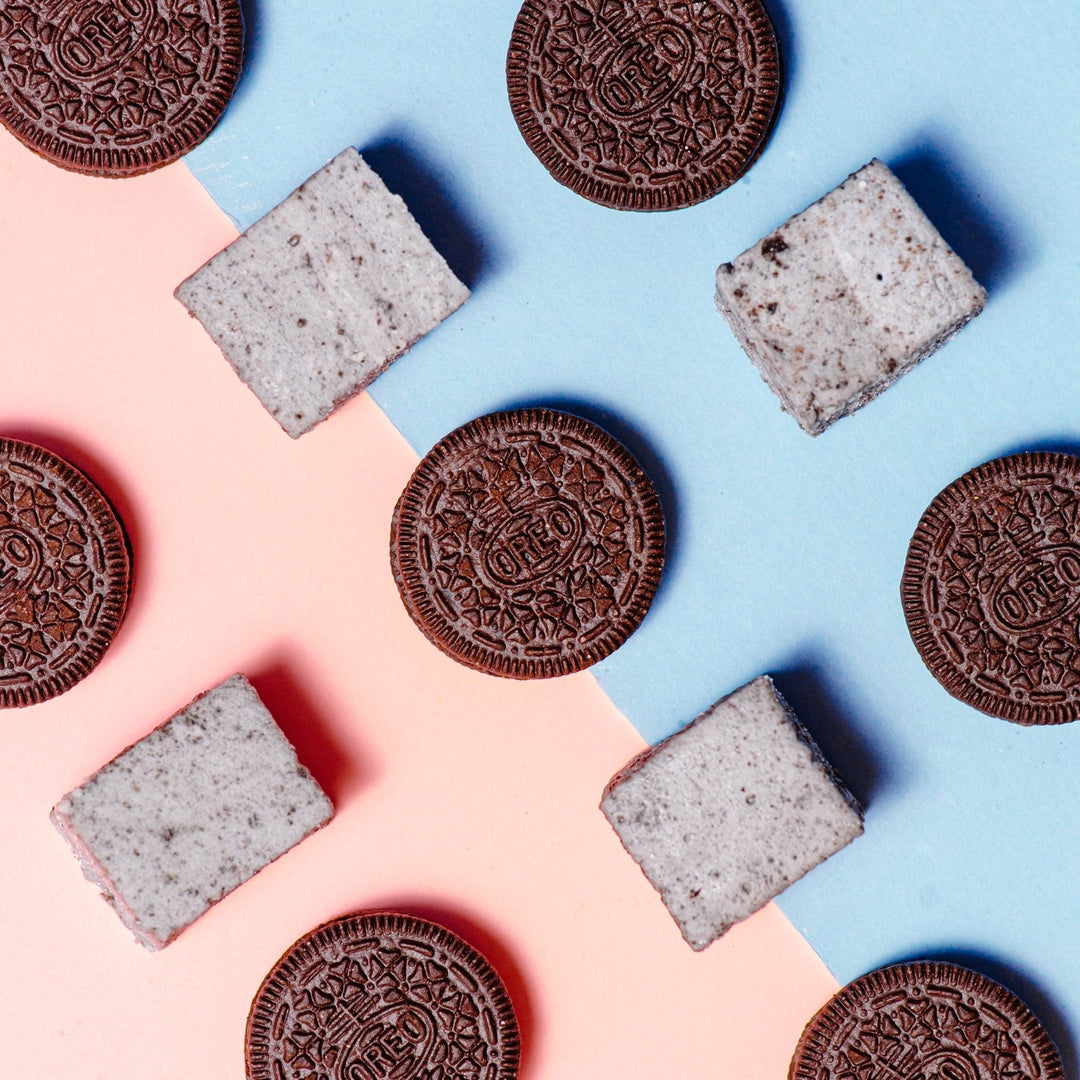 A grid of XO Marshmallow cookies and cream marshmallows alternating with Oreos against a half pink. half blue background. Even though Oreos are used in the photos, the marshmallows are gluten free.