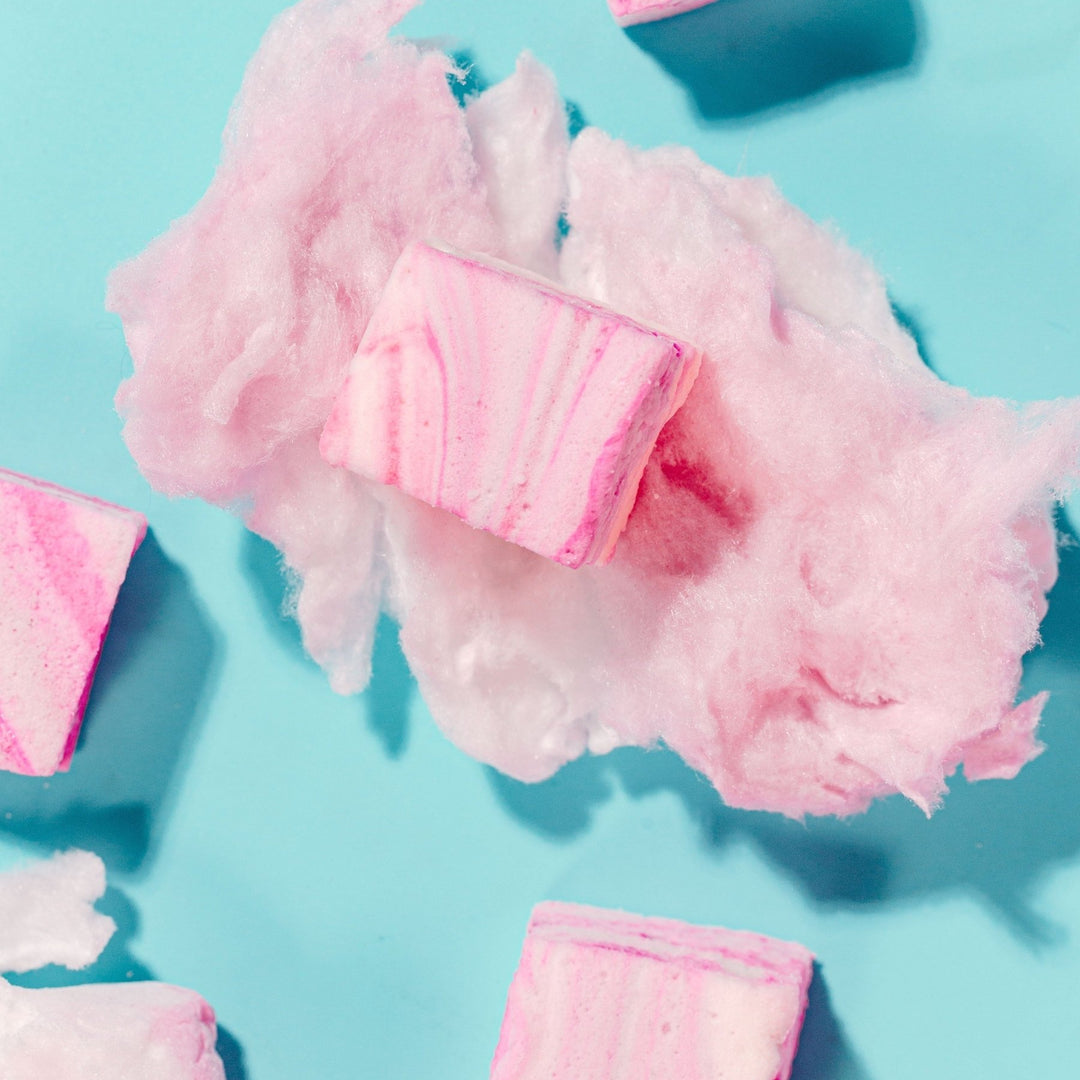 A handmade cotton candy gourmet marshmallow sitting on top of a cloud of pink cotton candy against a blue background