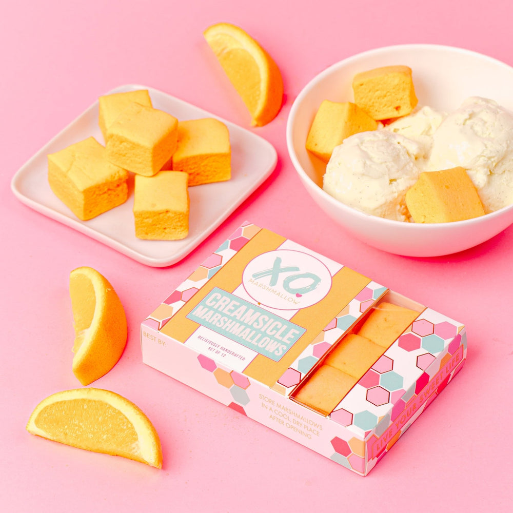 a box of xo marshmallow creamsicle marshmallows on its side next to loose orange slices and a bowl of ice cream