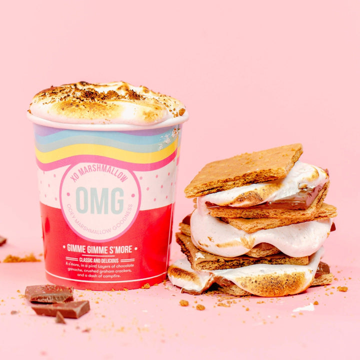 A pint of s'mores flavored gourmet marshmallow creme to the left of a stack of 3 s'mores that are overflowing and gooey because they were made with fluff instead of traditional marshmallows 