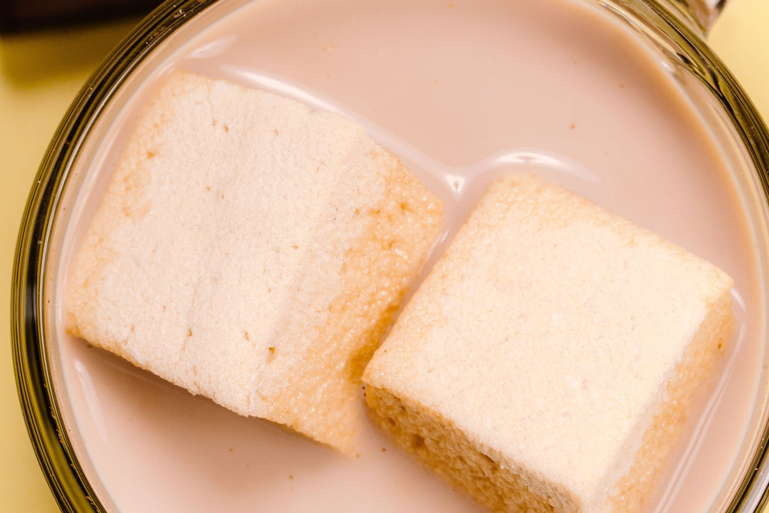 A super close up overhead shot of a glass mug full of hot chocolate with two XO Marshmallow gourmet hot chocolate marshmallows melting on top of it.
