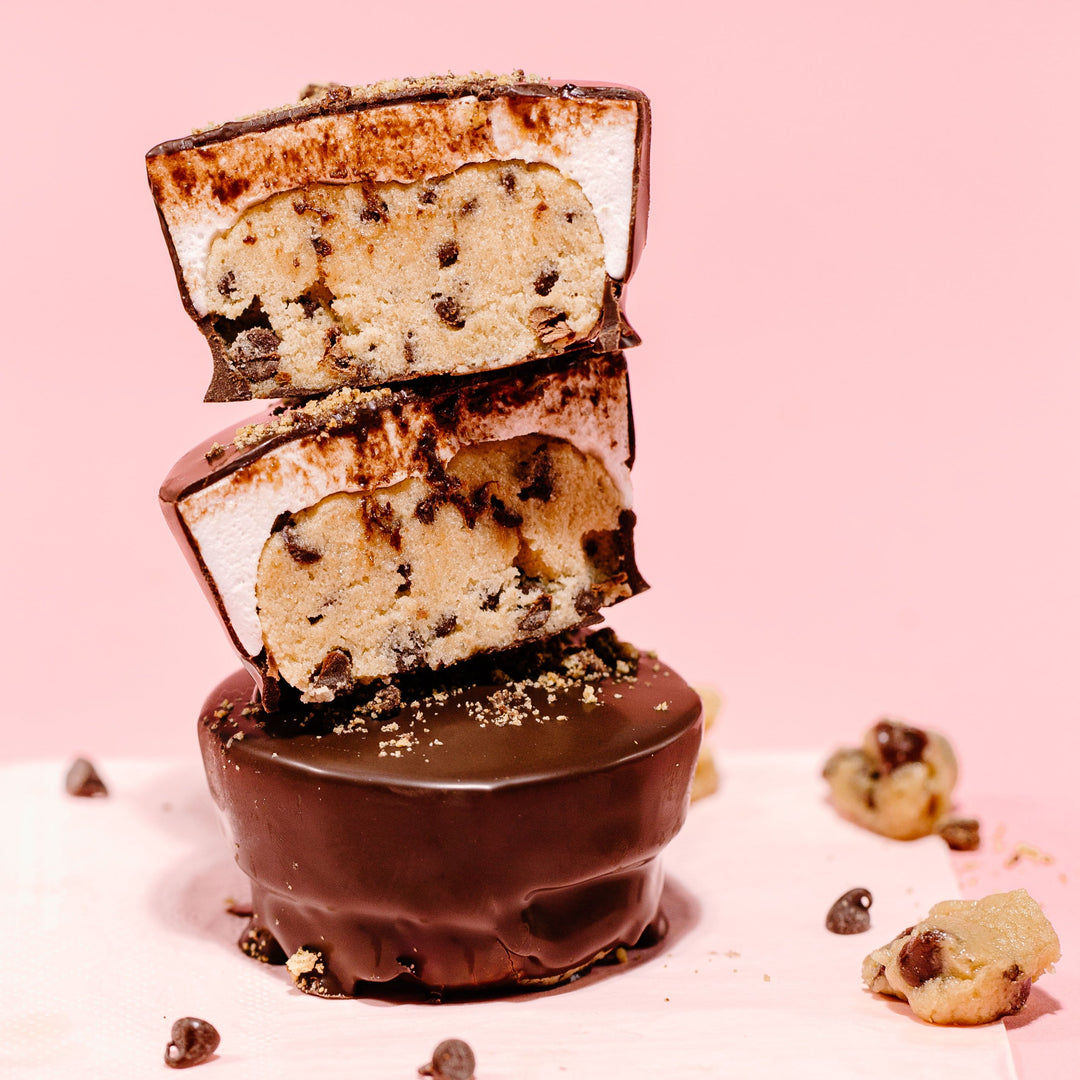 Stack of edible cookie dough cups with chocolate coating and marshmallow filling, with chocolate chips visible on the side.