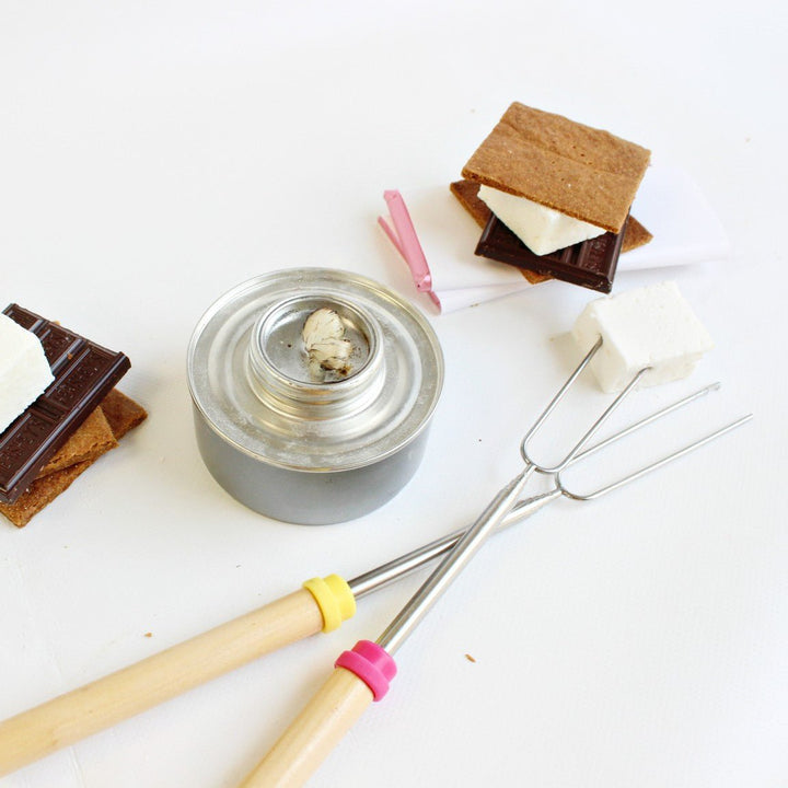 A set of 2 marshmallow roasting skewers next to a table top fire pit and a s'more.