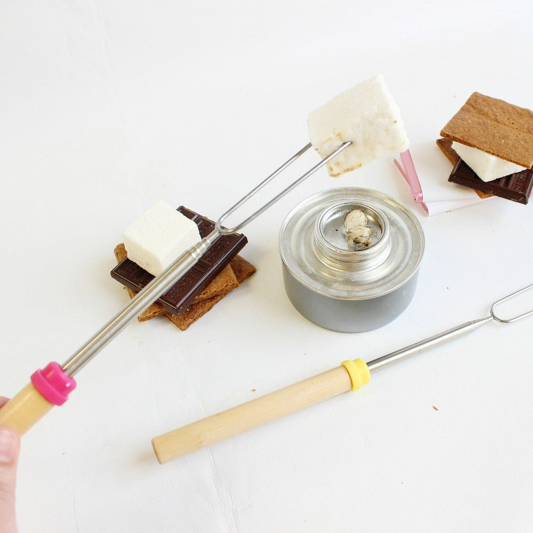 A marshmallow roasting stick with a marshmallow on it over a table top fire pit showing how you can use the sticks to roast XO Marshmallows.