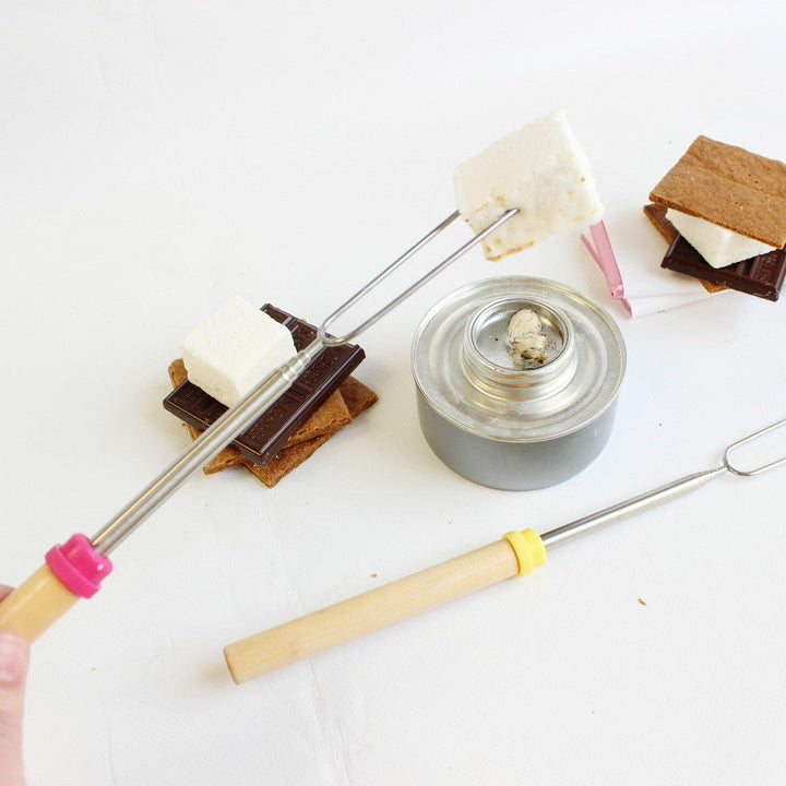 A marshmallow roasting stick with a marshmallow on it over a table top fire pit showing how you can use the sticks to roast XO Marshmallows.