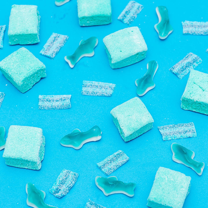 A variety of blue marshmallows and gummy candies spread out on a blue background.